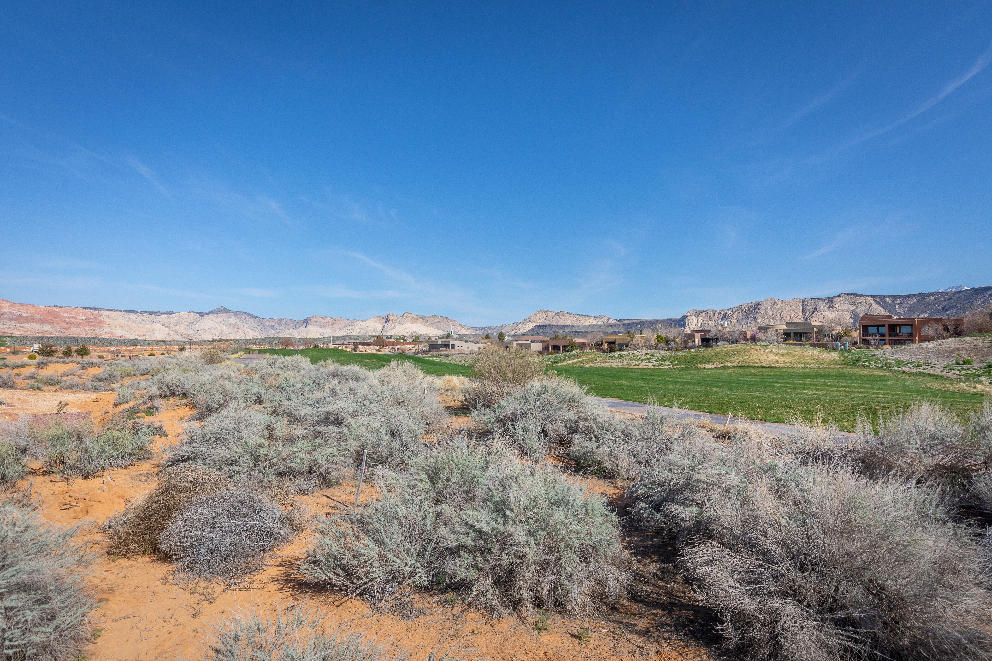 Paisaje desértico con vegetación escasa, un campo de golf y edificios modernos al fondo.