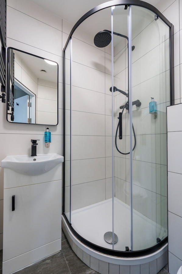 A modern bathroom with a glass-enclosed shower, a white sink, and a mirror.