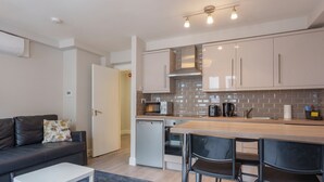 A modern kitchen with a microwave, toaster, and coffee maker, a dining area with bar stools, and a sofa with a decorative pillow. - The Temple Bar Lane (Dublin)