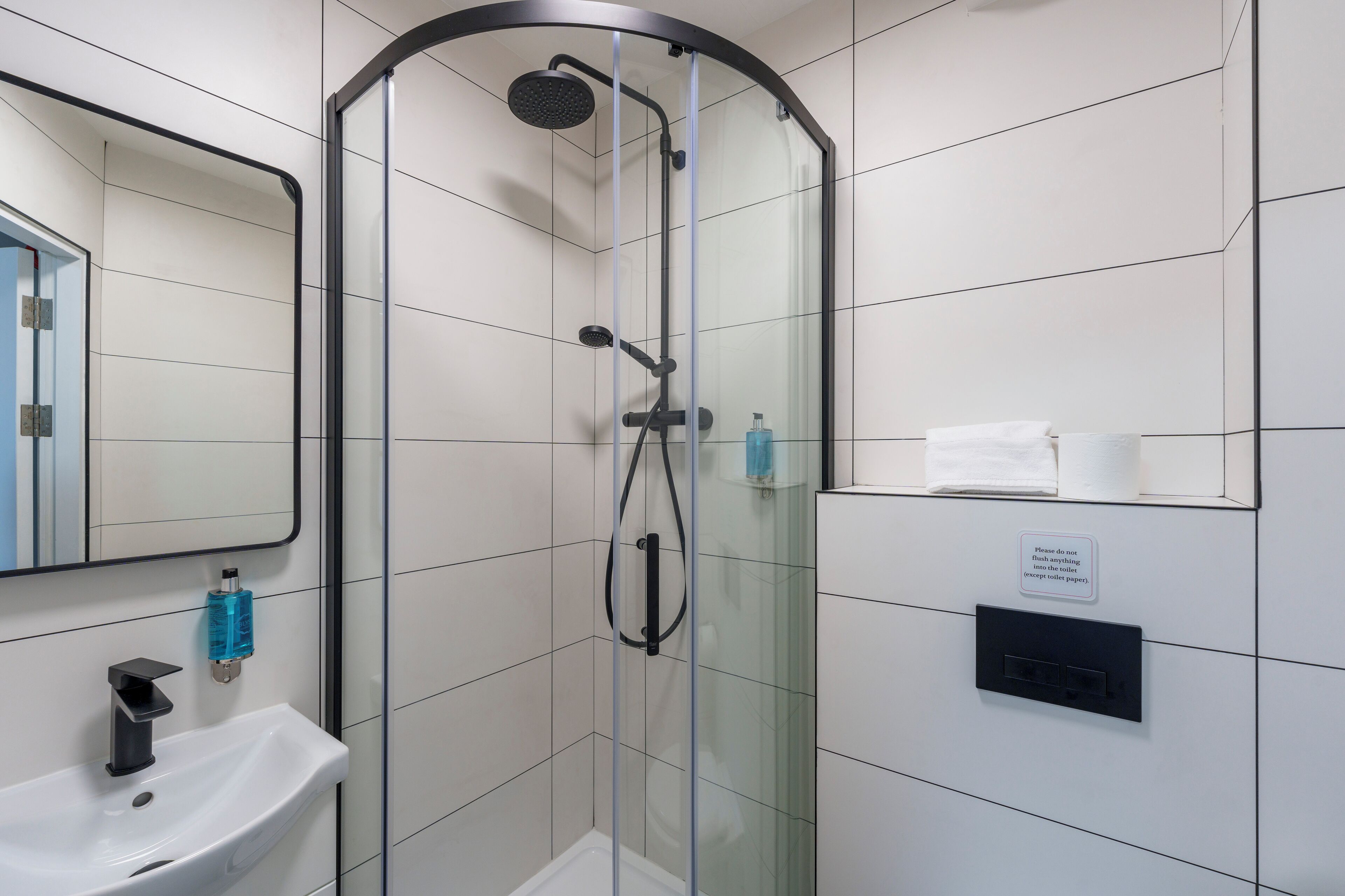 A modern bathroom with a glass-enclosed shower, a white sink, and a mirror.