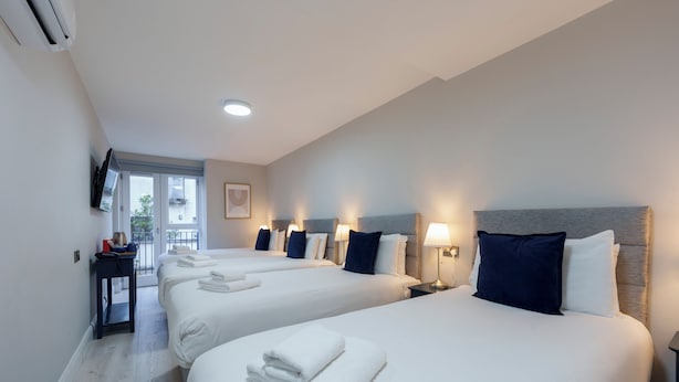 A hotel room with three beds, each with white linens and a folded towel. There is a small table with a lamp and a TV mounted on the wall. - The Temple Bar Lane (Dublin)