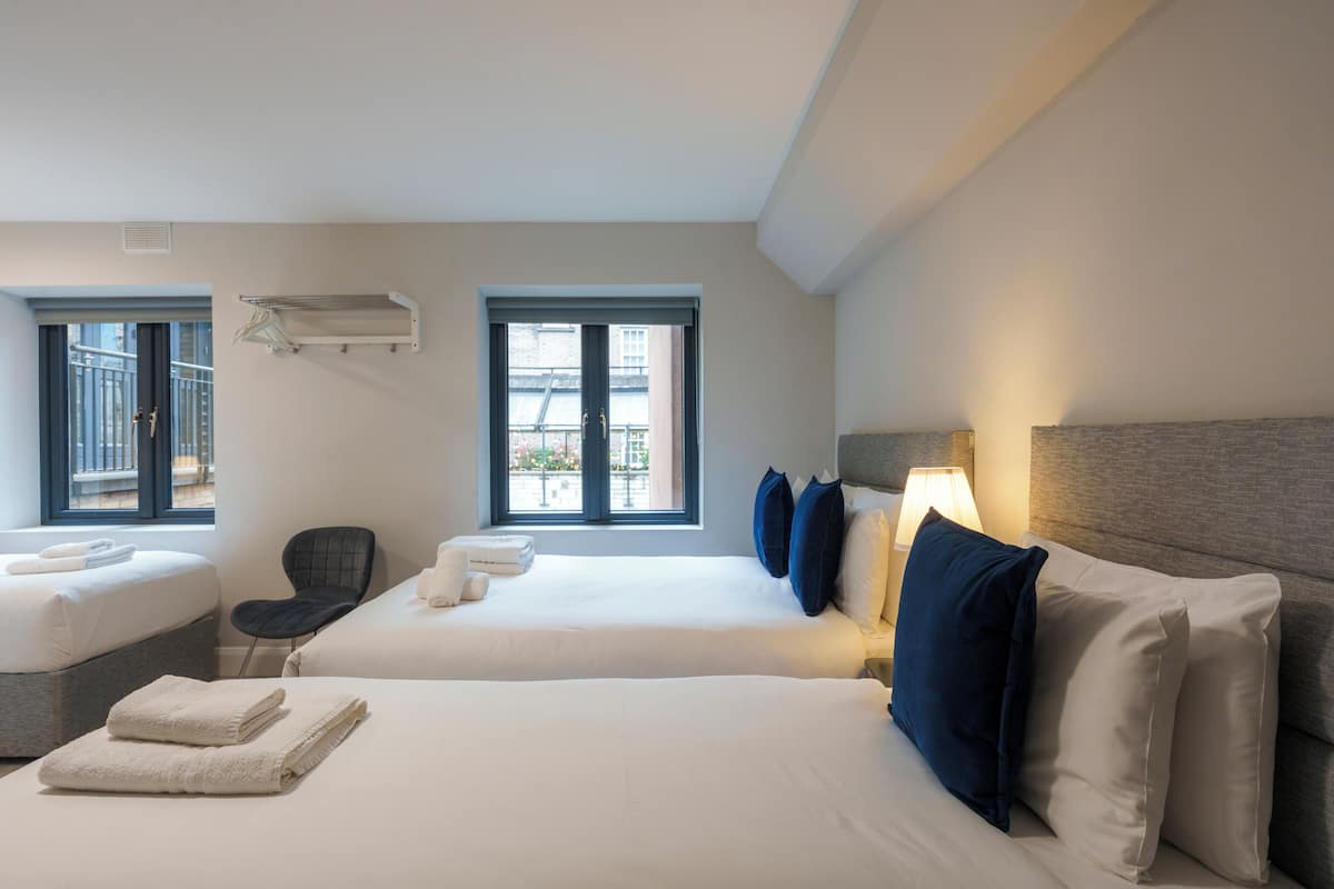 A hotel room with two beds, a chair, a window, and a lamp.