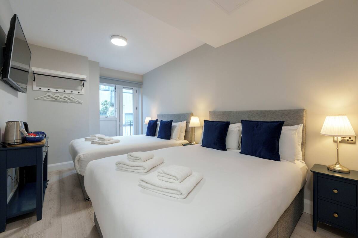 A hotel room with two beds, a TV, a desk, and a lamp.