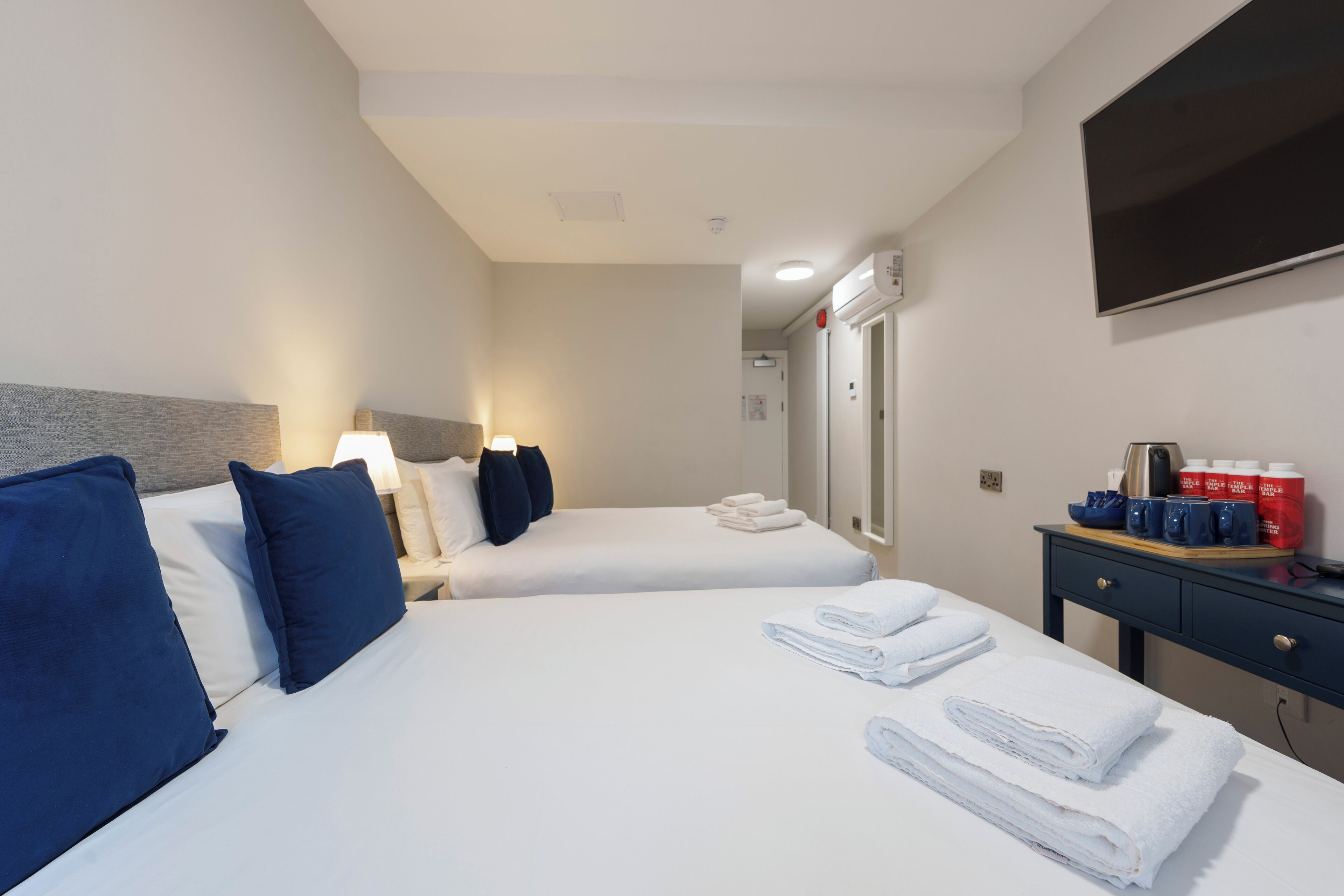 A hotel room with two beds, a desk with a flat-screen TV, and a mirror.