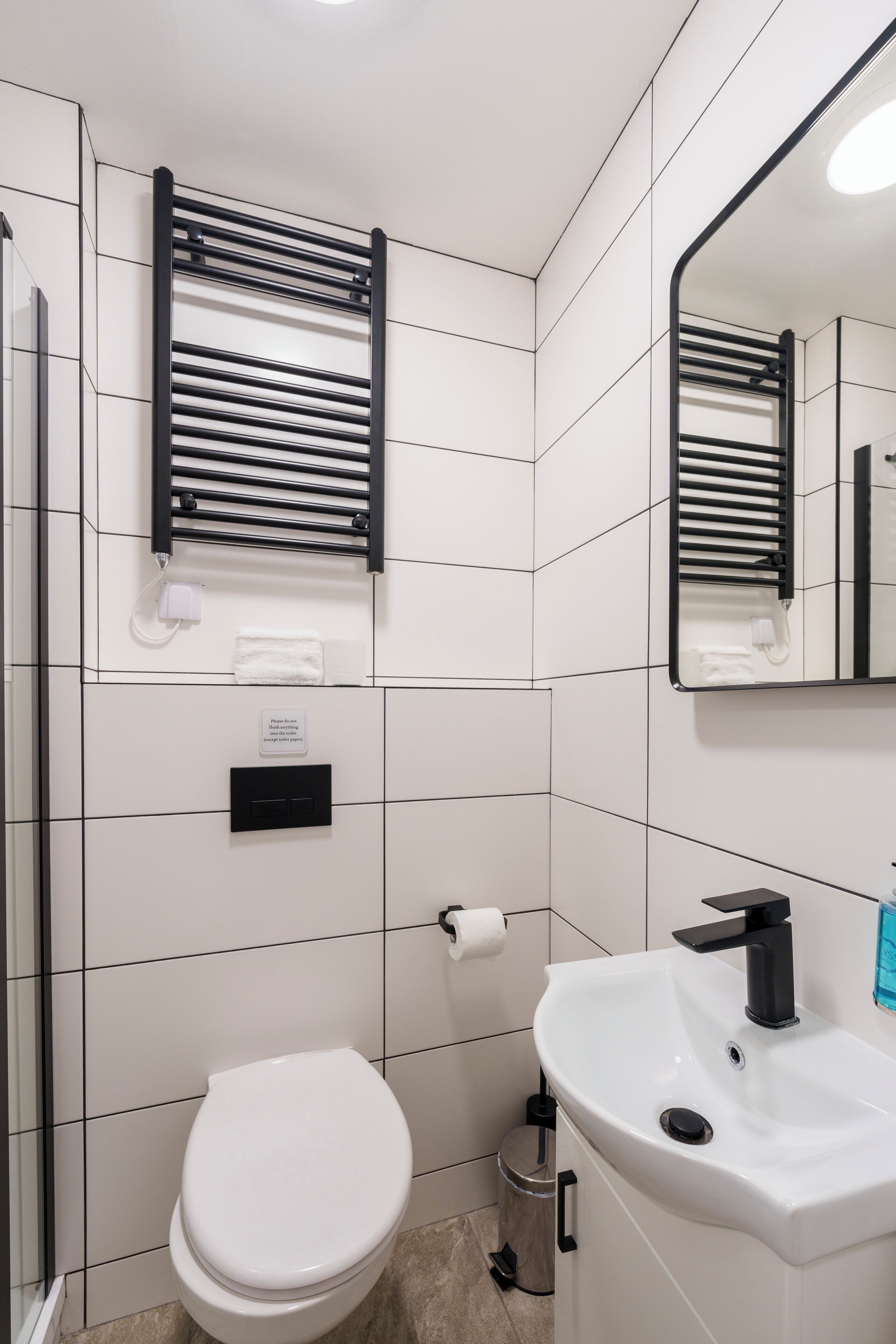 Ein modernes Badezimmer mit einer weißen Toilette, einem Waschbecken mit schwarzem Wasserhahn und einem Handtuchhalter mit Handtuch.