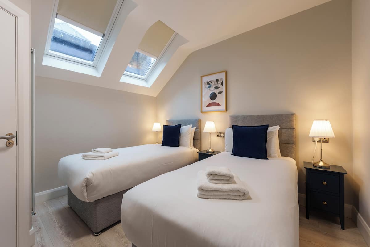 A hotel room with two beds, a skylight, a painting, and bedside lamps.