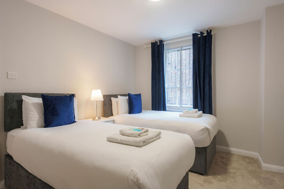 A hotel room with two beds, a window with curtains, a lamp, and a view of the city.
