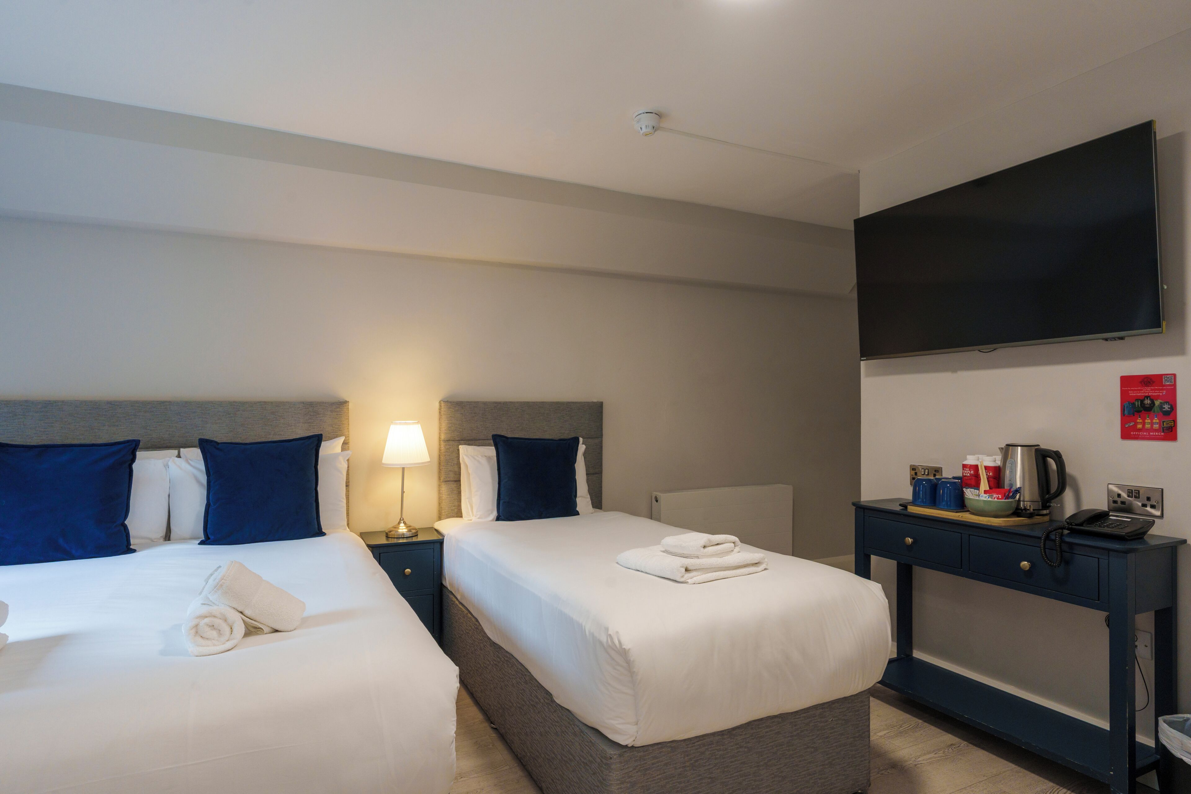 A hotel room with two beds, a TV, a desk with a kettle, and a coffee machine.