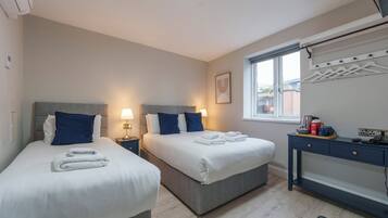 Habitación de hotel con dos camas, un escritorio, una ventana y un tendedero en la pared.