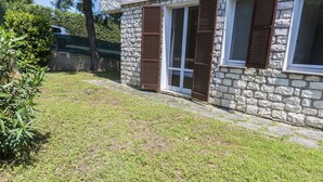 Un bâtiment en pierre avec une cour verdoyante, un arbre et une voiture en arrière-plan.