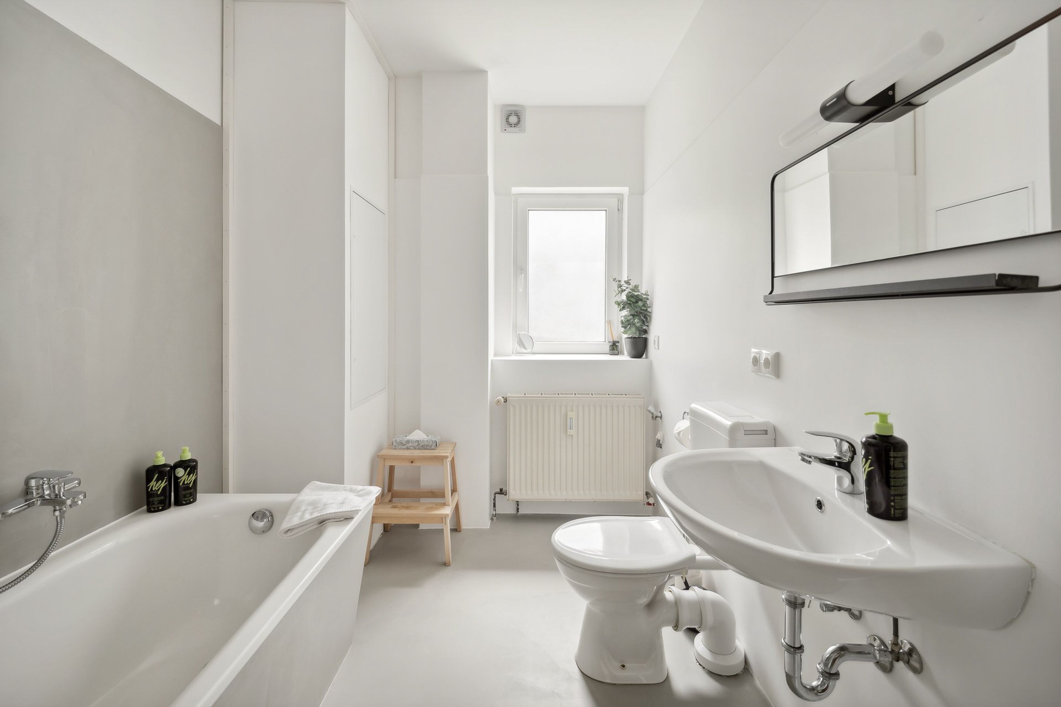 Ein modernes Badezimmer mit Badewanne, Toilette und Waschbecken. Auf der Fensterbank stehen ein kleiner Holzschemel und ein Blumentopf.