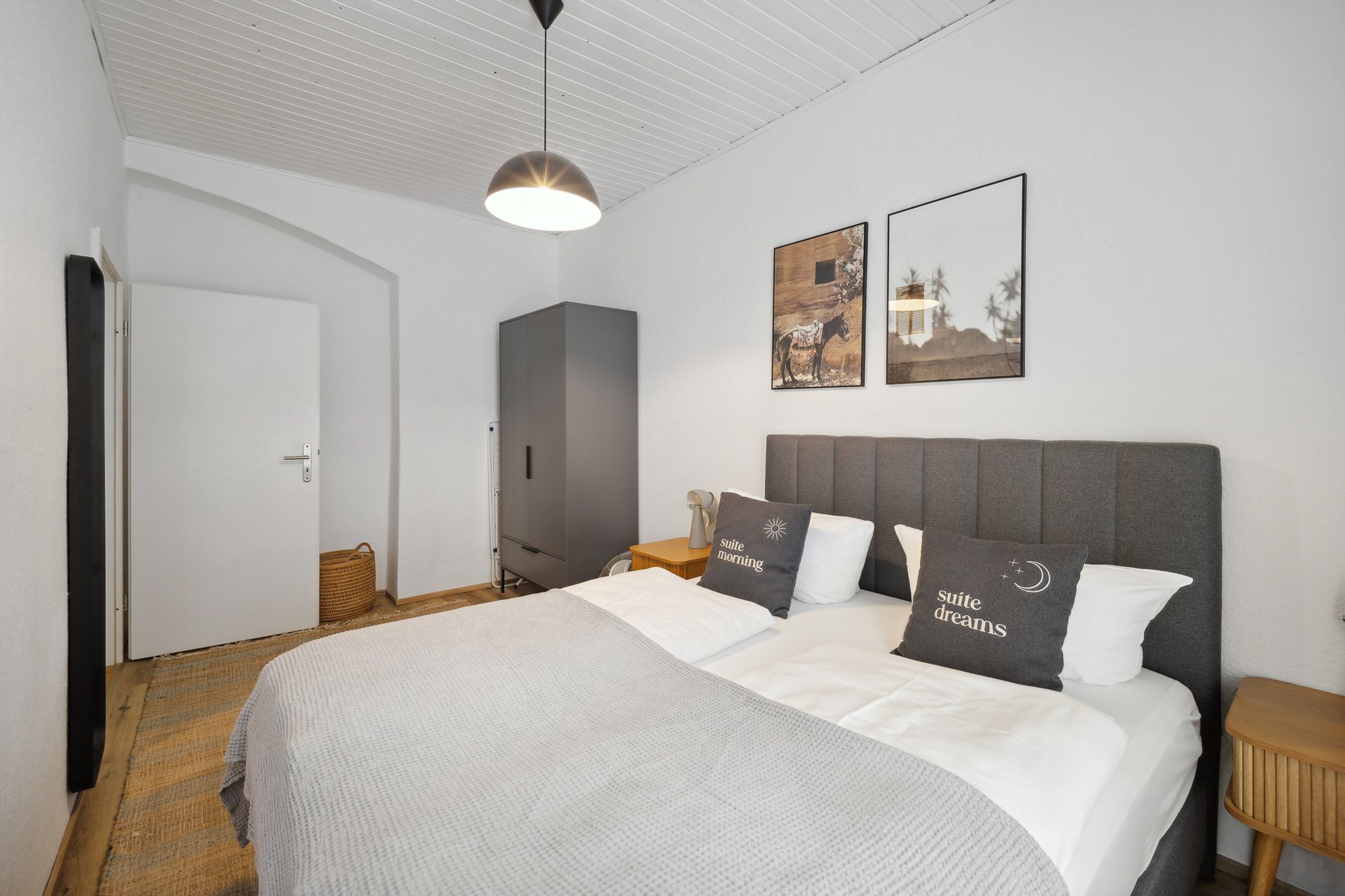 A neatly arranged bedroom with a large bed, a bedside table, a wardrobe, and two framed pictures on the wall.