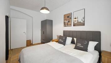 A neatly arranged bedroom with a large bed, a bedside table, a wardrobe, and two framed pictures on the wall.