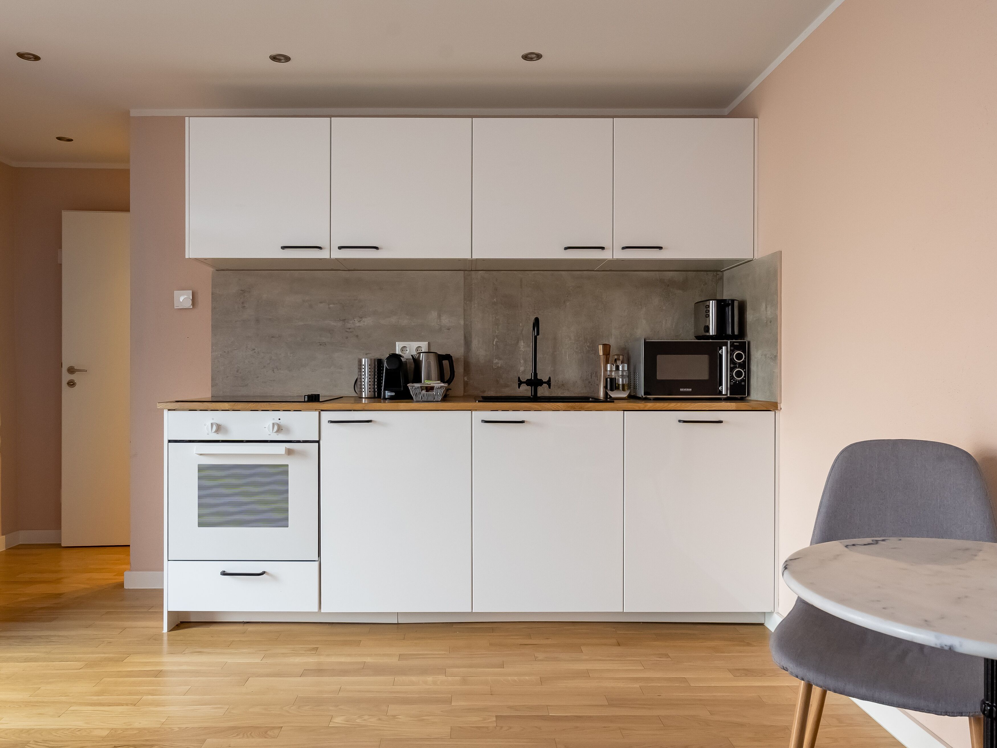 Una cucina moderna con mobili bianchi, forno a incasso, microonde e macchina del caffè.