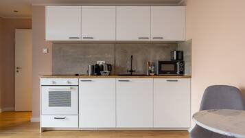 Una cucina moderna con mobili bianchi, forno a incasso, microonde e macchina del caffè.