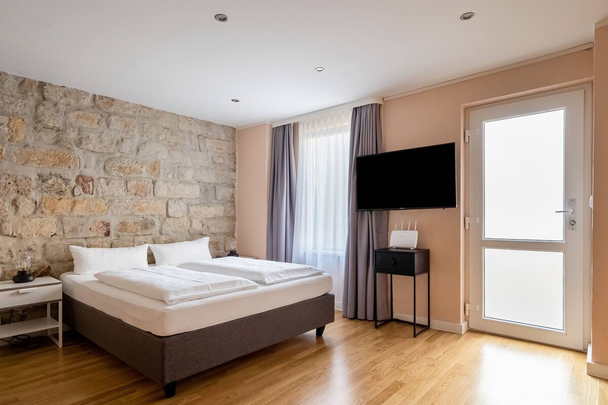 A modern bedroom with a stone wall, a bed, a bedside table, a flat-screen TV, and a sliding glass door.