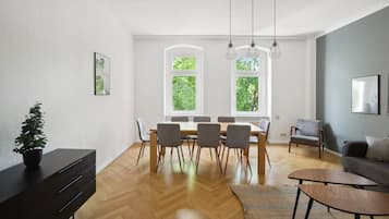 A modern living room with a dining area, large windows, and a view of greenery.