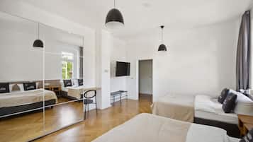 A modern hotel room with a large mirror, a flat-screen TV, a wooden floor, and a bed with a headboard.