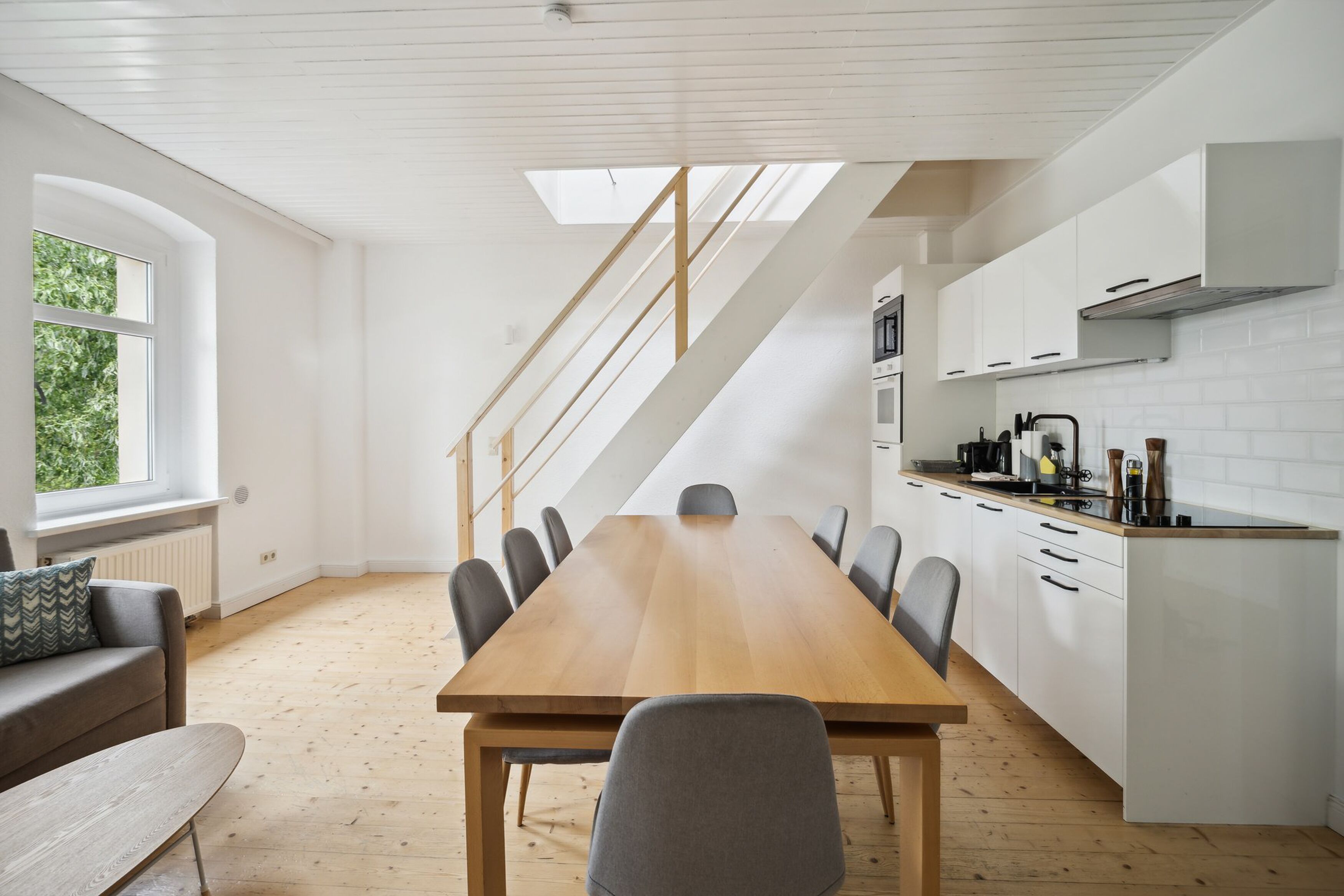 A modern kitchen with a wooden table and chairs, white cabinets, and a skylight.