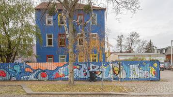 A multi-story building with a blue facade, a tree in front, and a colorful mural on the fence.