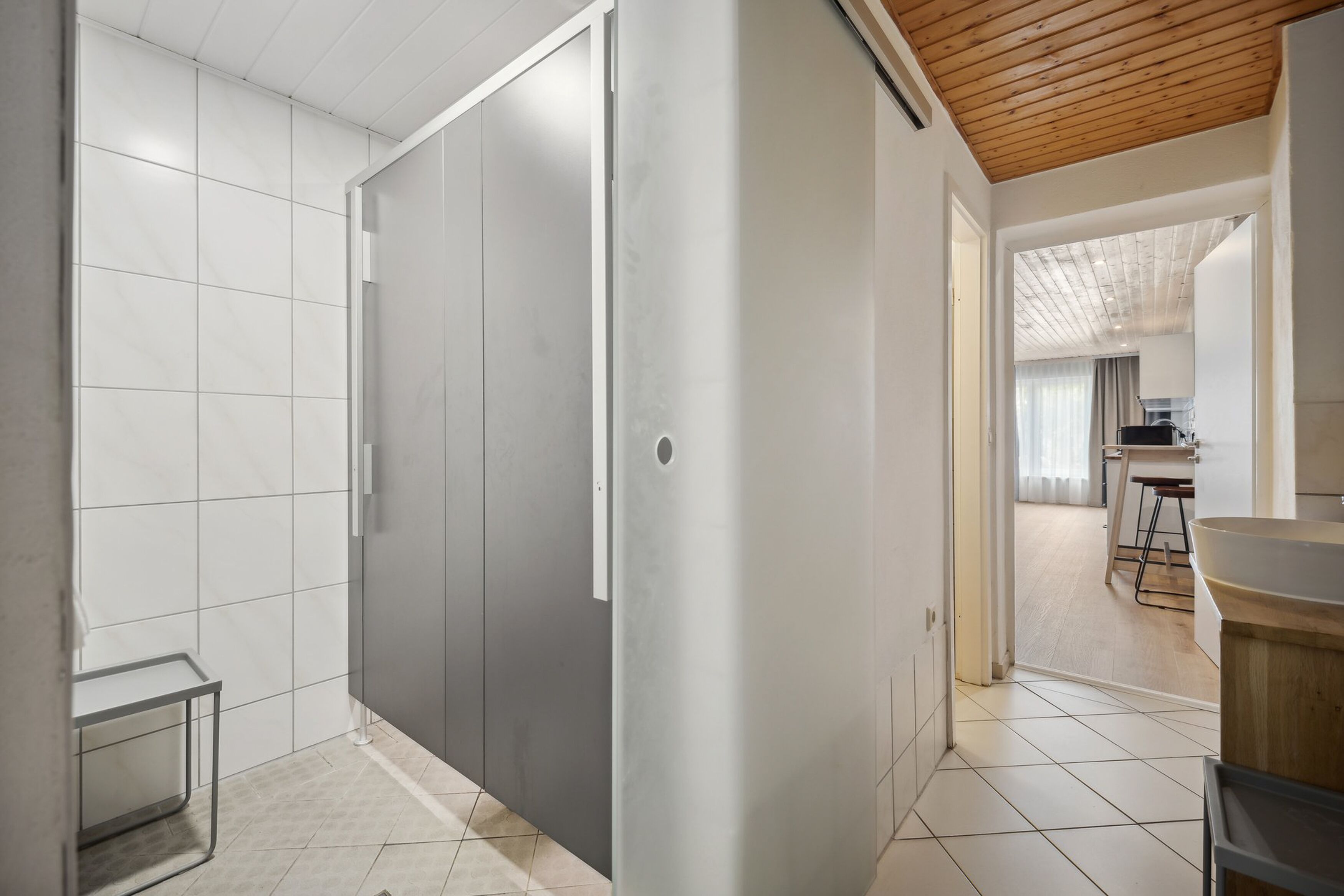 Ein modernes Interieur mit einer Schiebetür, gefliestem Boden und einem durch eine geöffnete Tür einsehbarer Küchenbereich.