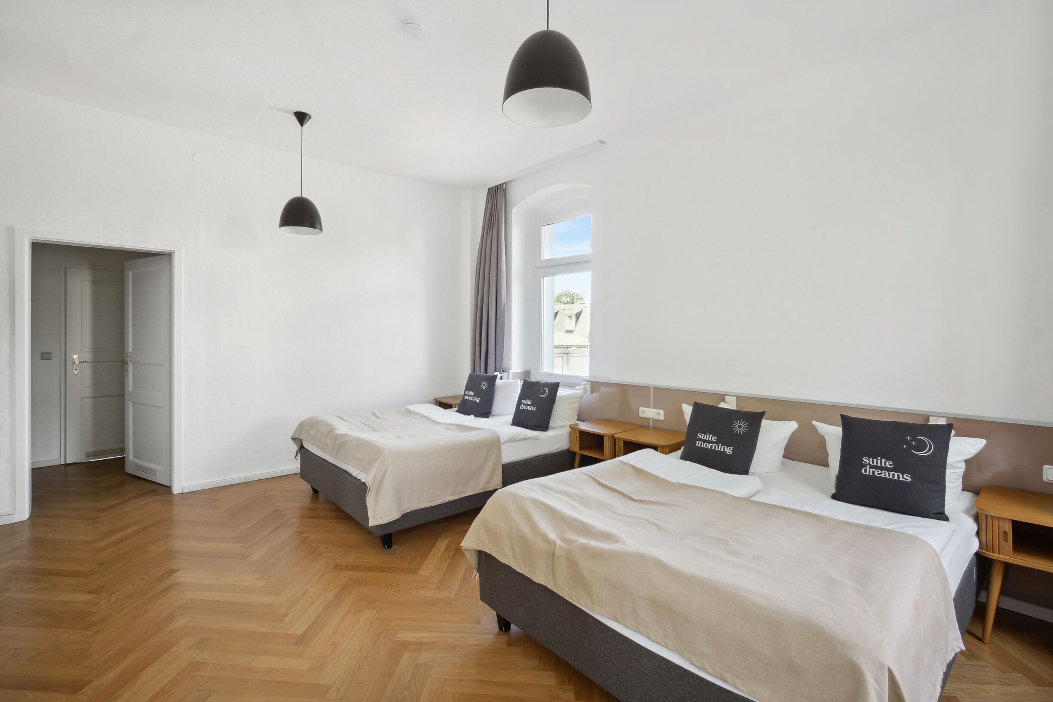 A hotel room with two beds, a wooden floor, a large window, and a hanging light fixture.