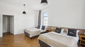 A hotel room with two beds, a wooden floor, a large window, and a hanging light fixture.