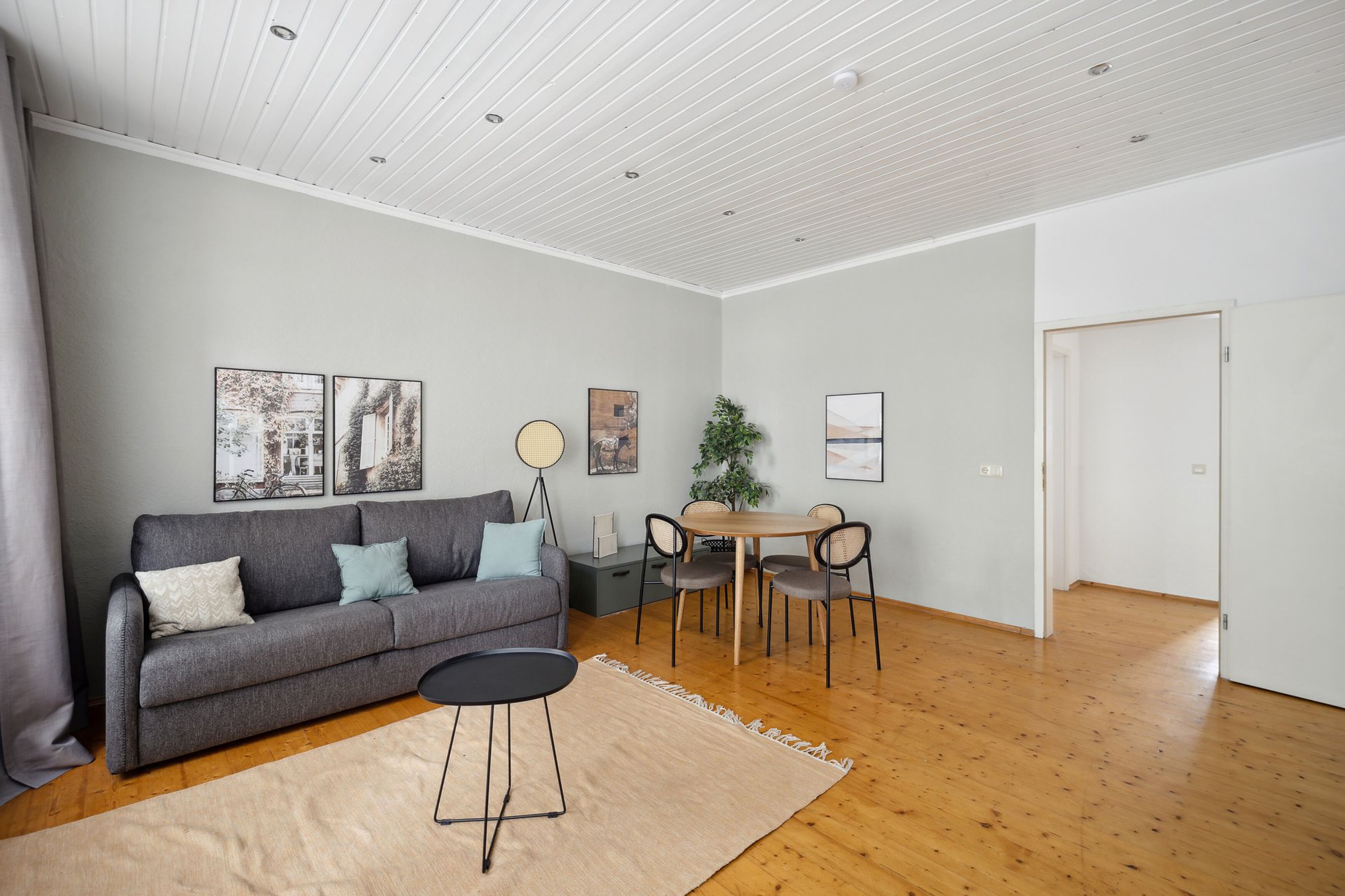Un salon moderne avec un canapé gris, une table ronde et un coin repas.