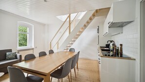 Una cocina moderna con una escalera de madera, un comedor con una mesa grande y sillas, y vistas al exterior con vegetación.