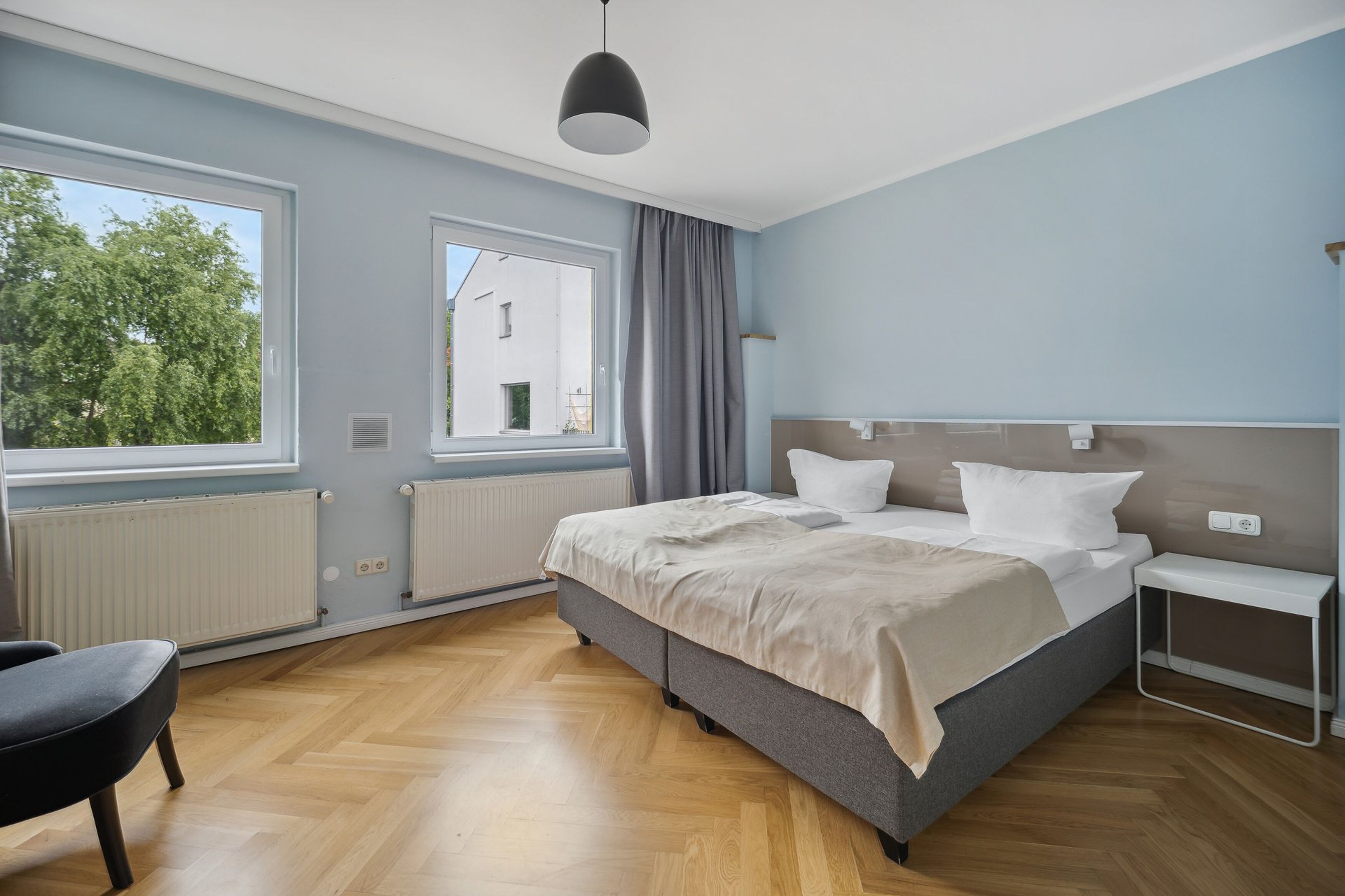 A modern bedroom with a large bed, a bedside table, a chair, and a window with curtains.
