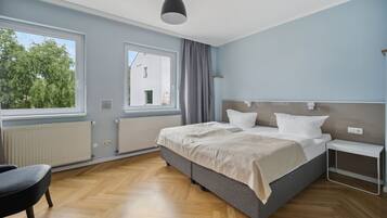 A modern bedroom with a large bed, a bedside table, a chair, and a window with curtains.