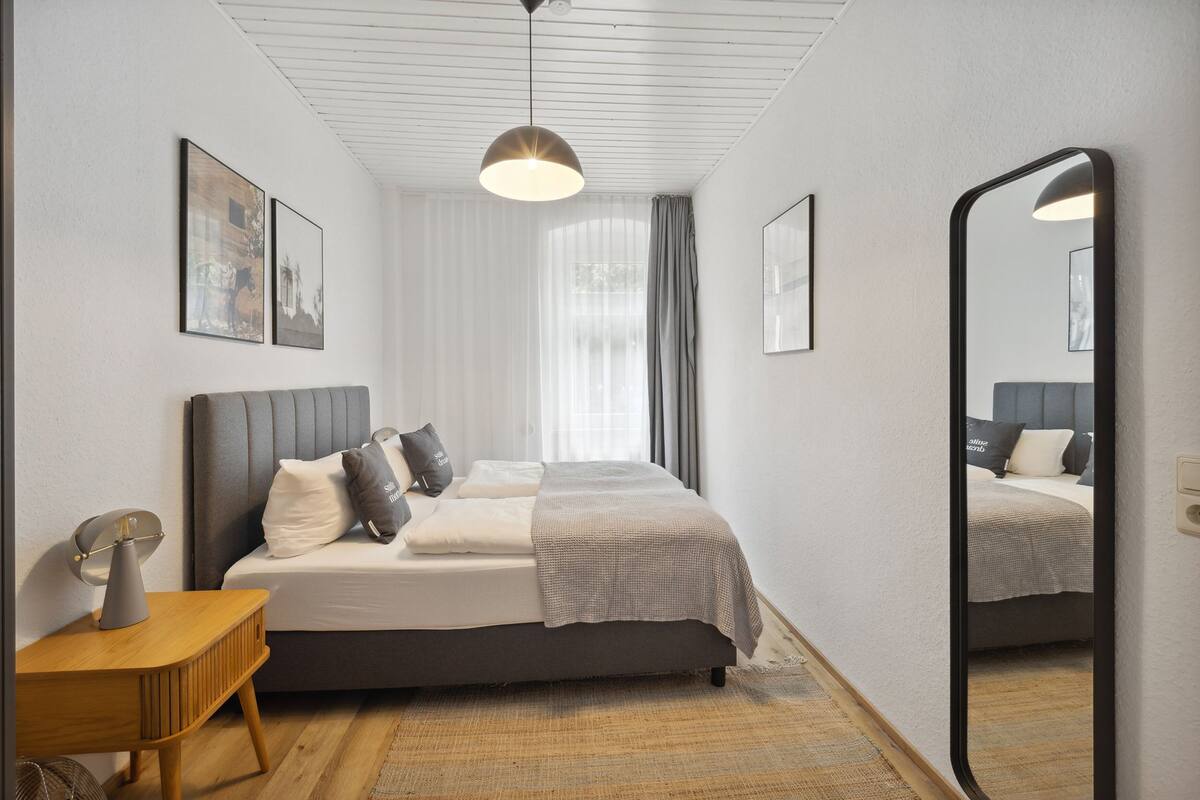 A modern bedroom with a bed, bedside table, and a large mirror.