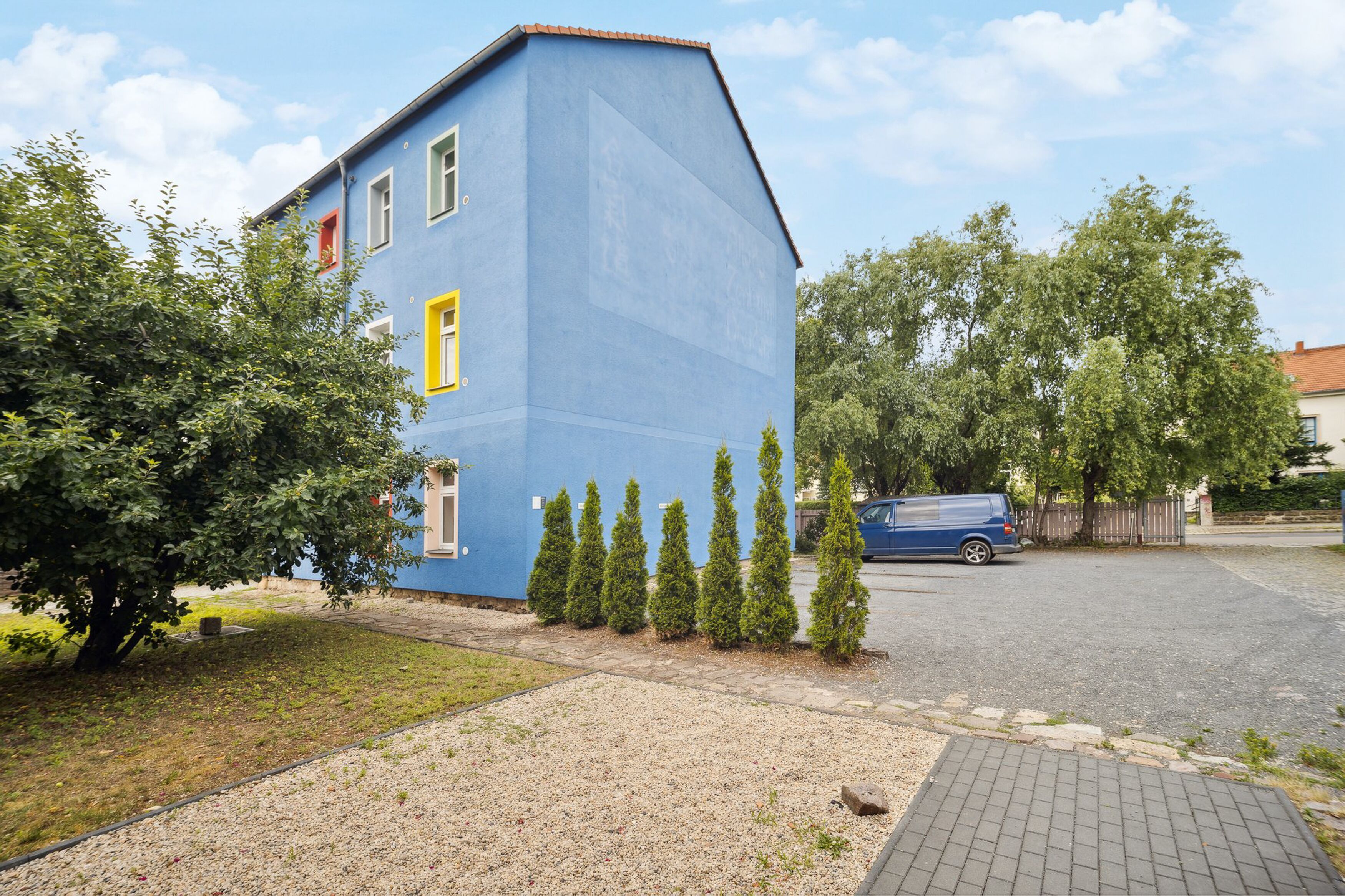 A blue building with a sloped roof, a driveway, and a parked van.
