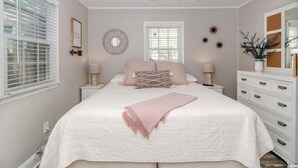 Een slaapkamer met een bed, nachtkastjes, een plafondventilator, een raam met jaloezieën, een spiegel en een dressoir.