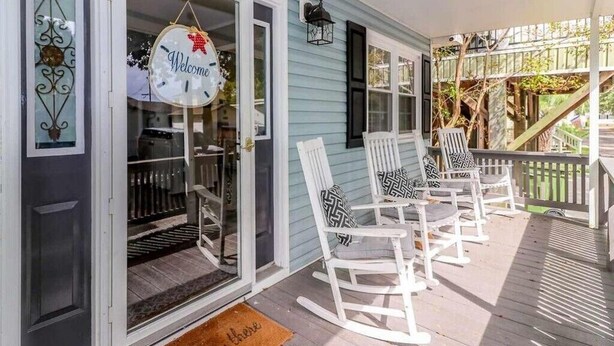 Een veranda met witte schommelstoelen en een 'Welcome' bord.