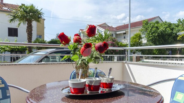 A balcony with a table set for two, featuring a vase with red roses, two cups, and a tray. - Apartmani Marinović - Vodice (Vodice)