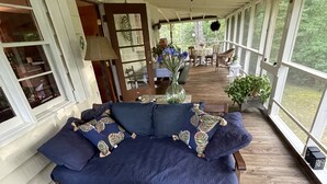 En inglasad veranda med en blå soffa, ett runt bord med ett ljus och utsikt över omgivningen.