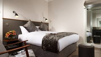 A modern hotel room with a large bed, bedside lamps, a small table with a vase of flowers, and a mirror in the corner.