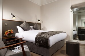 A modern hotel room with a large bed, bedside lamps, a small table with a vase of flowers, and a mirror in the corner.