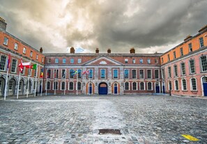 A historic building with a central courtyard, multiple flags, and a cobblestone ground.