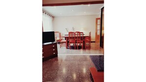 Un coin repas avec une table et des chaises, un téléviseur posé sur une commode, et une porte donnant sur une autre pièce.