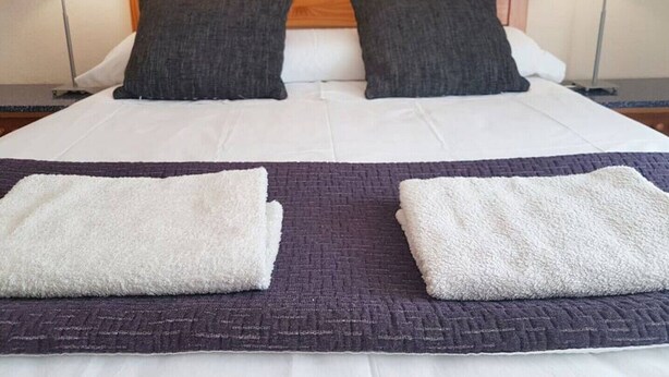 Un lit bien fait, avec deux oreillers, une tête de lit en bois et deux lampes de chevet.