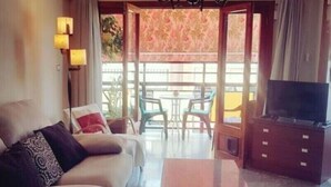 Une chambre d’hôtel avec un canapé, une table basse, un téléviseur et un balcon équipé d’une table et de chaises.