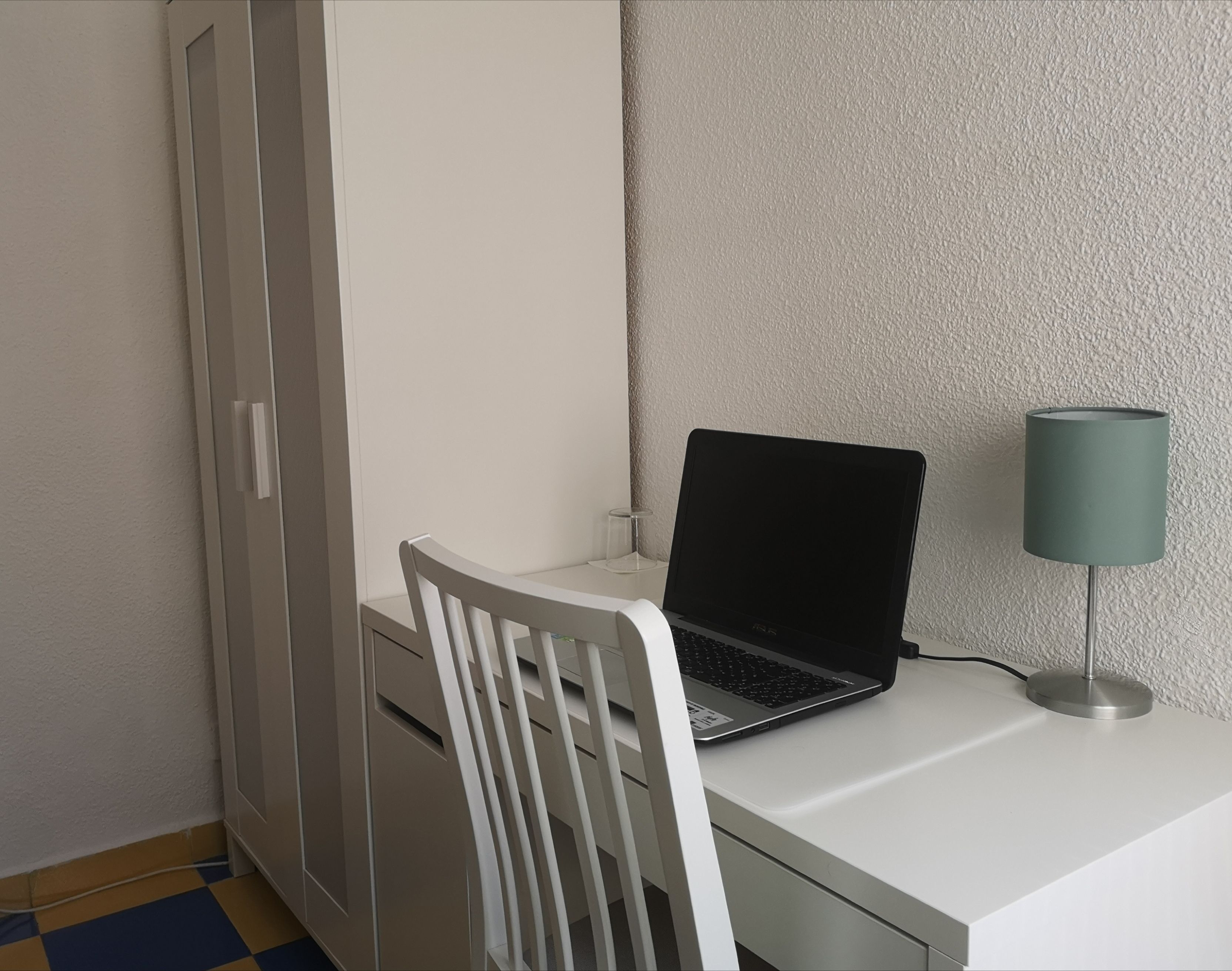 A small, white desk with a laptop and a lamp.