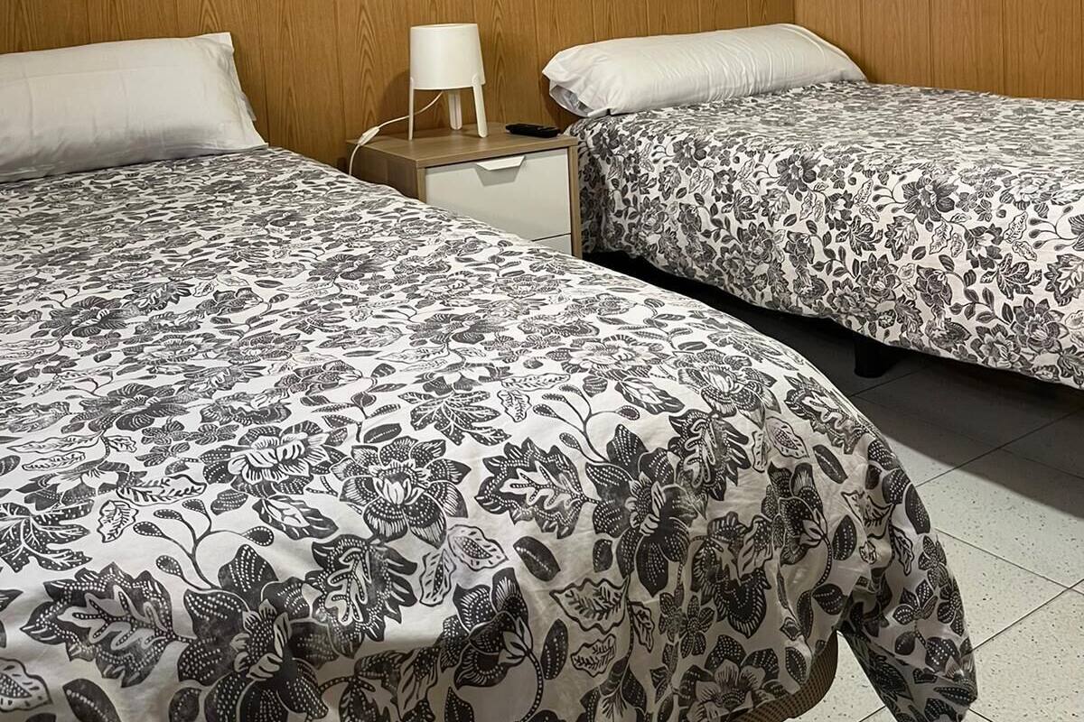 A hotel room with two beds, wooden headboard, a nightstand with a lamp, a painting on the wall, and a mirror.