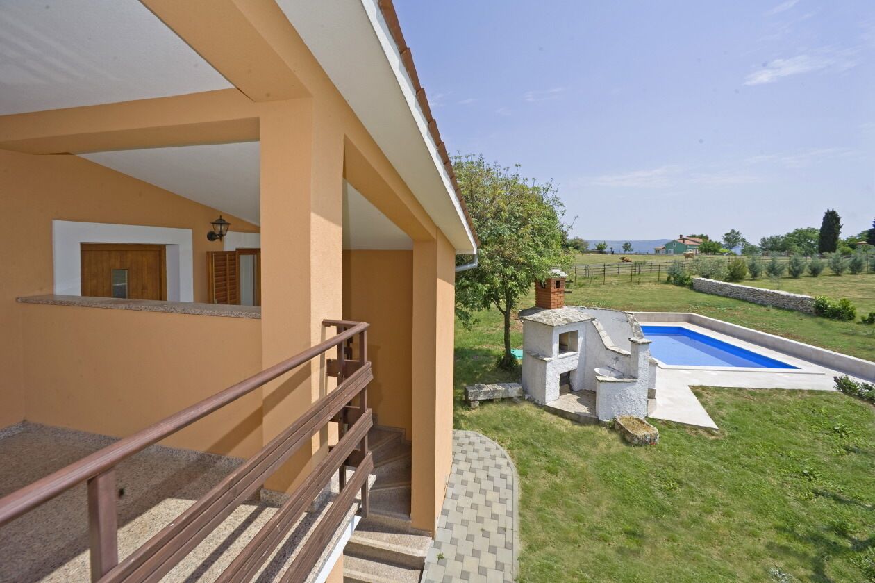 A residential building with a covered outdoor area, a swimming pool, and a view of the surrounding landscape.