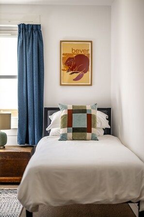 Ein Schlafzimmer mit einem Bett, einem blauen Vorhang, einem Wandbild und einem Nachttisch.