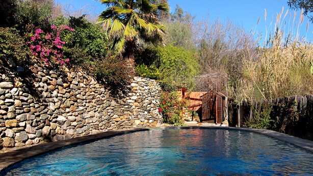 A swimming pool with a stone wall and a wooden structure in the background. - Casa Champasak, Alpujarra Granada, VTAR/GR/01097 (Las Barreras - Órgiva)