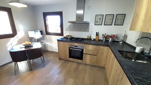 A modern kitchen with wooden cabinets, a gas stove, an oven, and a sink. There is a dining area with a table and chairs. - Casa Champasak, Alpujarra Granada, VTAR/GR/01097 (Las Barreras - Órgiva)