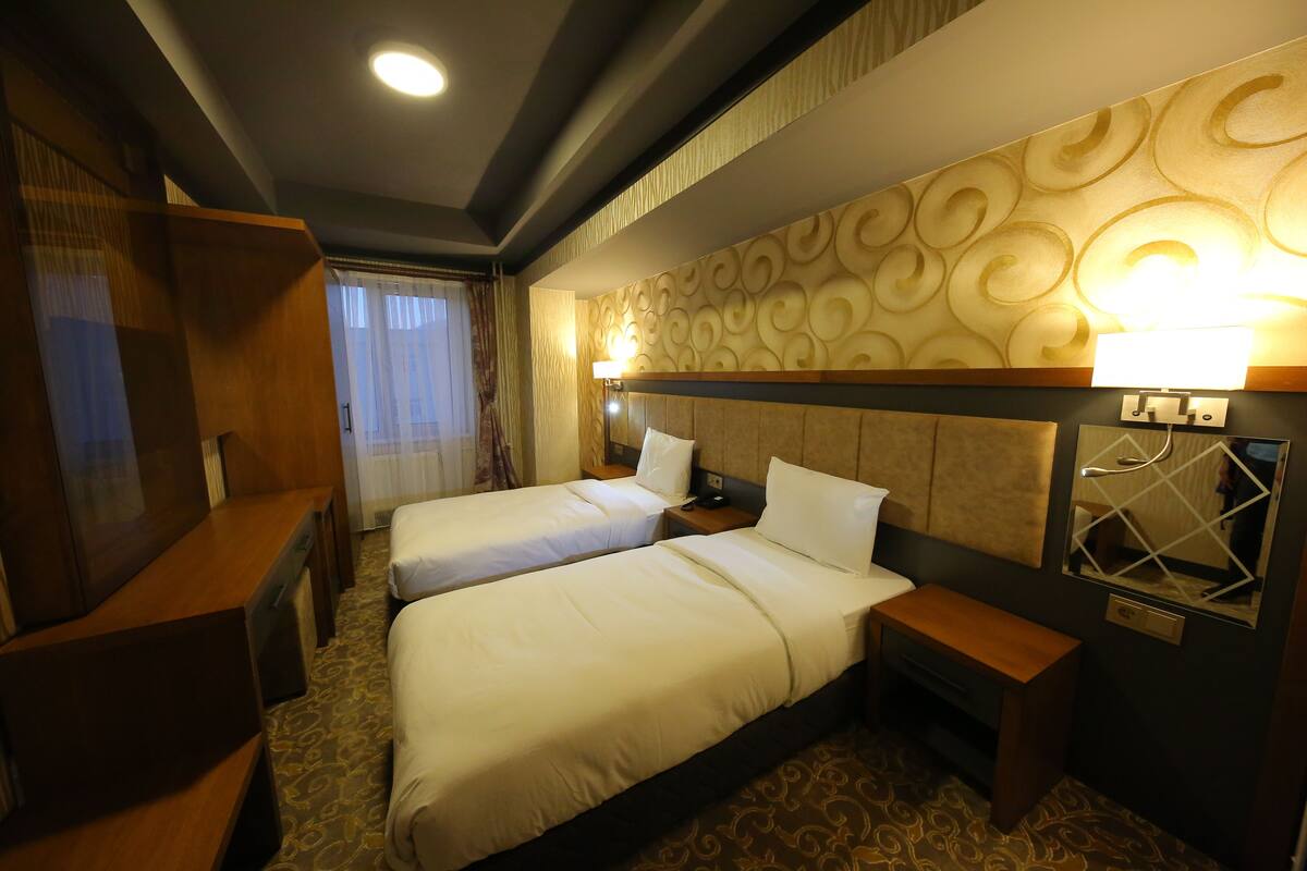 A hotel room with two beds, a wooden desk, a mirror, and a patterned wall.